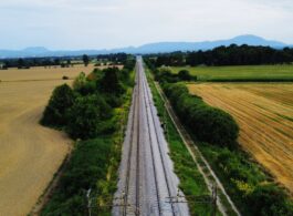 vista de drone, ferrovia seguindo até o horizonte com plantação e vegetação de ambos os lados