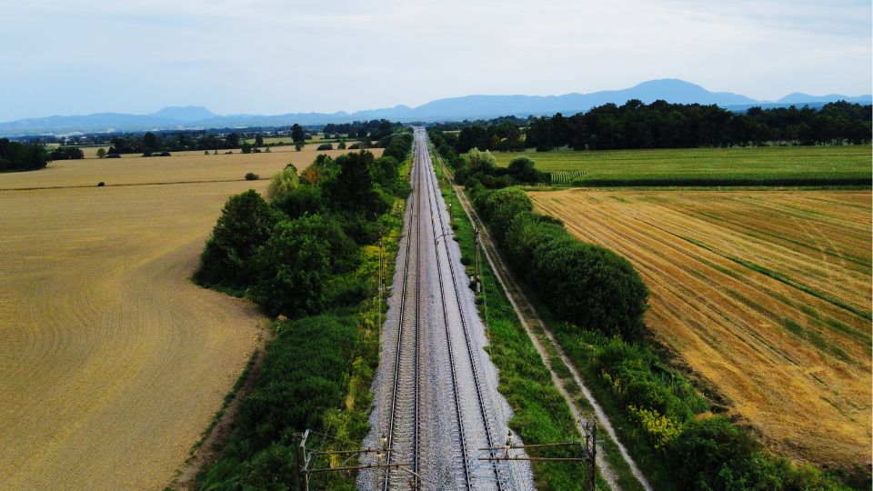 vista de drone, ferrovia seguindo até o horizonte com plantação e vegetação de ambos os lados