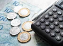 calculadora e reais brasileiros na mesa com cédulas e moedas junto de uma caneta prata