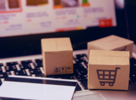 Notebook com mini caixas de papelão em cima do teclado com um cartão de crédito do lado, na tela mostra um site de compras