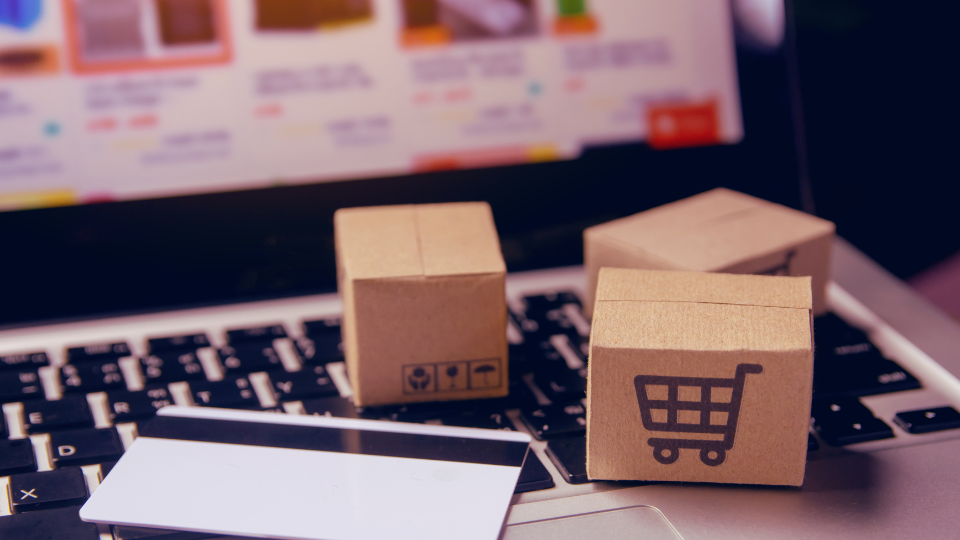 Notebook com mini caixas de papelão em cima do teclado com um cartão de crédito do lado, na tela mostra um site de compras